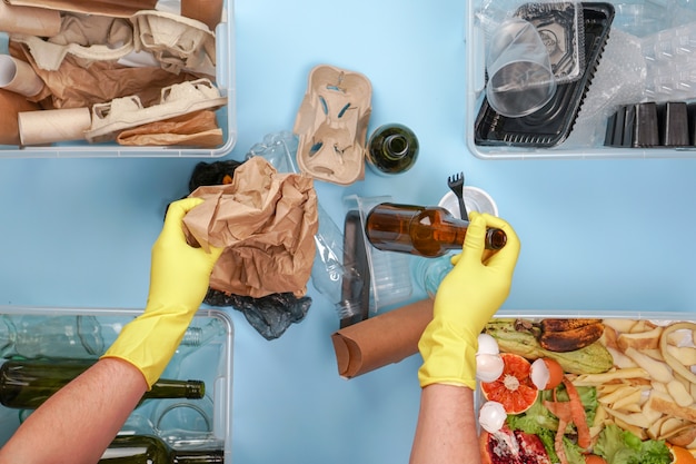 Male hands in yellow gloves hold paper and glass trash on a blue background