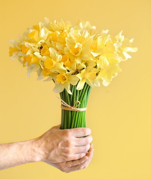 Male hands on yellow wall with a bouquet of yellow daffodils.