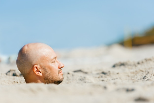 Testa del maschio sopra la sabbia sulla spiaggia con il corpo sotto terra