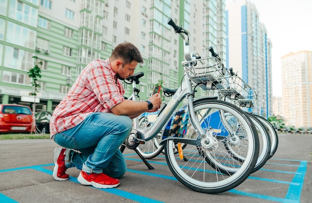 明るいカソ服を着た男性ハイカーが路上で共有自転車に乗って散歩します自転車フレームのQRコードをスキャンしますシティバイクを借りて街を移動します