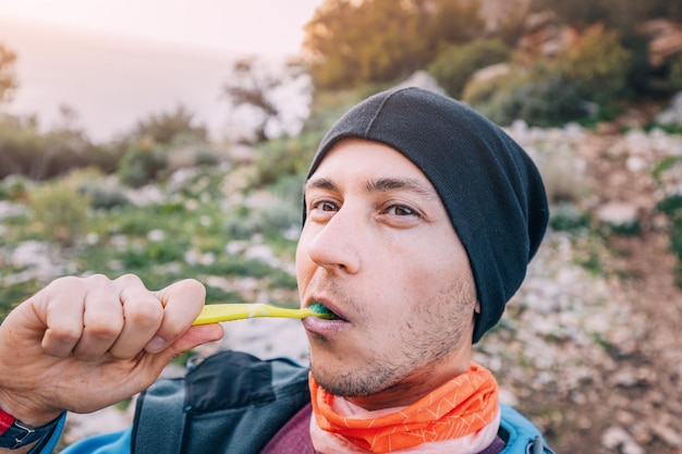 a male hiker in hat brushes his teeth at a camping site Hygiene and dental health in the woods