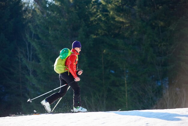 가문비나무 배경에서 스키를 타고 여행하는 배낭을 메고 있는 남성 등산객 활동적인 겨울 휴가