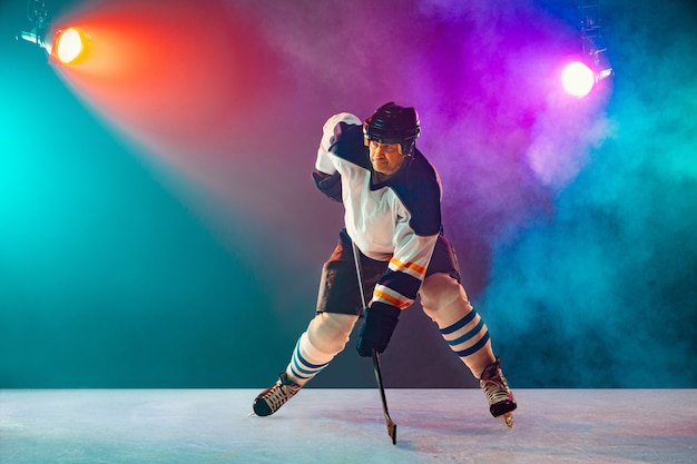Male hockey player on ice court and dark neon background, sport