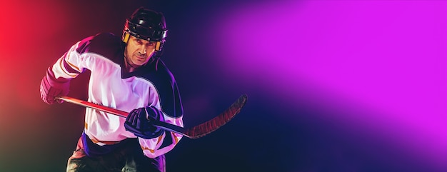 Фото Хоккеист-мужчина с клюшкой на ледовой площадке и темном неоновом фоне