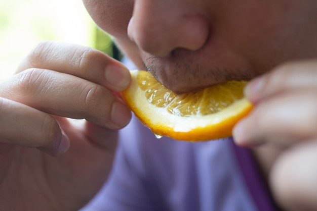 Maschio tenere e mangiare la fetta di frutta tropicale arancione per sano e rinfrescare in estate