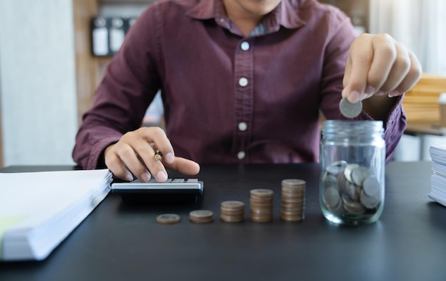 Male holding coins putting in glass with using calculator to calculate concept saving money for finance accounting