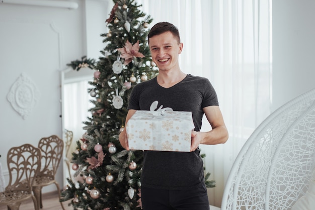 Мужчина держит подарочную коробку и улыбается. Рождество . Красивый мужчина в рубашке с подарочной коробкой