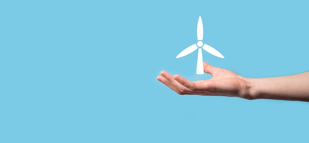 Male holding an icon of a windmill that produces environmental energy on blue surface.