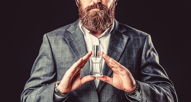 Male holding up bottle of perfume. Man perfume, fragrance. Perfume or cologne bottle and perfumery, cosmetics, scent cologne bottle, male holding cologne. Masculine perfume, bearded man in a suit