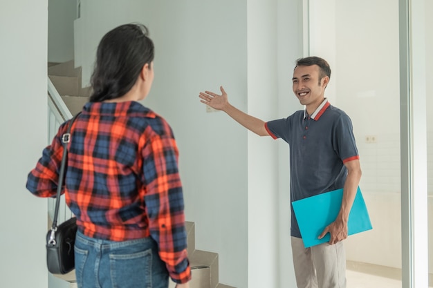 Застройщик мужского пола жестом предлагает клиентам подняться по лестнице, чтобы осмотреть комнаты в доме