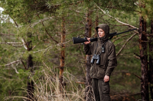 Male hunter with binoculars ready to hunt holding gun and walking in forest