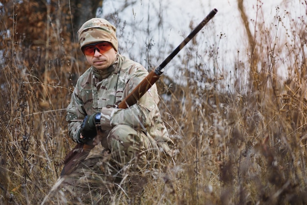 A male hunter with a gun while sitting takes aim at a forest