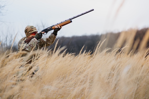 A male hunter with a gun while sitting takes aim at a forest