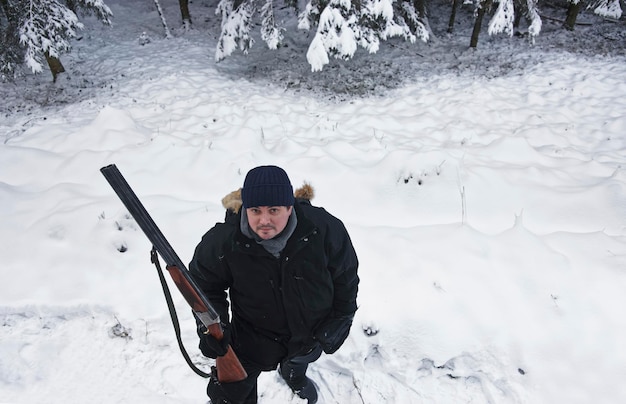 Foto cacciatore maschio con fucile nella foresta in inverno. la caccia e il tiro sono praticati da molti secoli. uno degli obiettivi è controllare la popolazione animale nella vita selvaggia