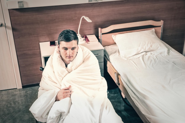 Male ill patient sitting on wheelchair covered with quilt in hospital ward. Healthcare concept