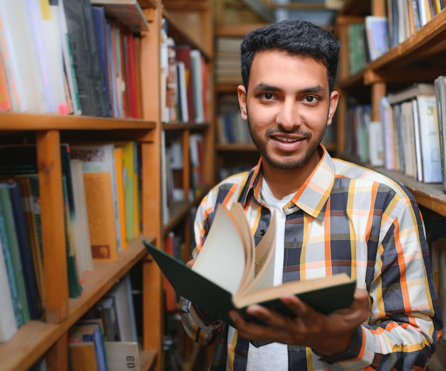 Male indian student at the library with book