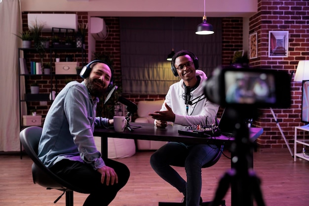 Male influencer using camera to record podcast conversation, filming talking show discussion in studio. Social media vlogger chatting and broadcasting live, meeting with happy guest.