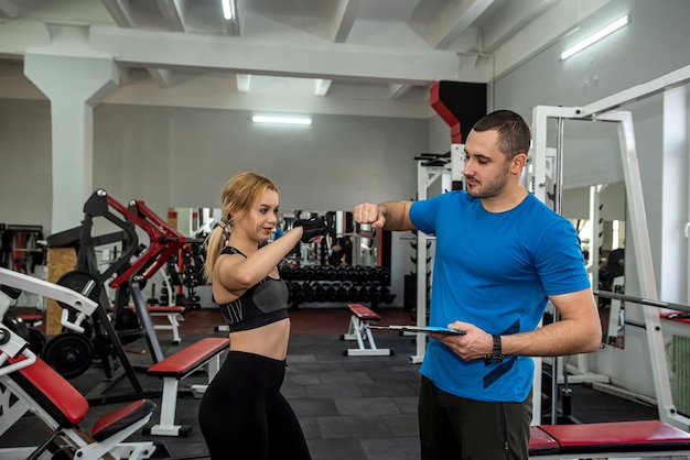 Male instructor exercising with his female client at gym woman working about the optimal training program