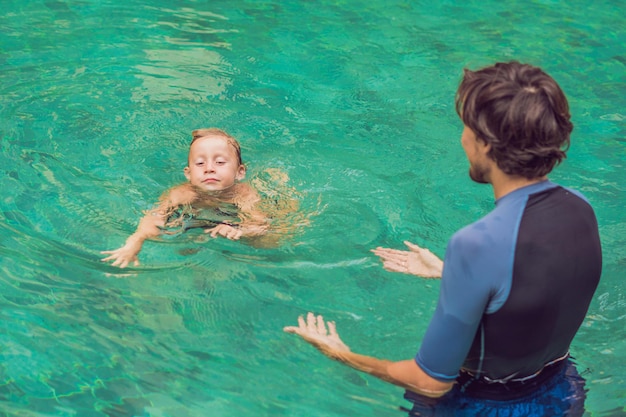 Male instructor swimming for children teaches a happy boy to swim in the pool