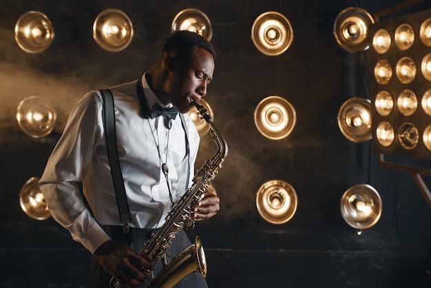 Male jazzman plays the saxophone on the stage with spotlights. Black jazz musician preforming on the scene