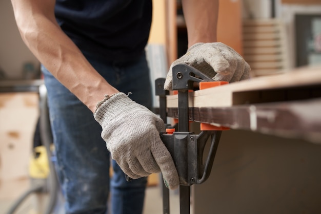 Male joiner in gloves clamps board in vice at workshop 