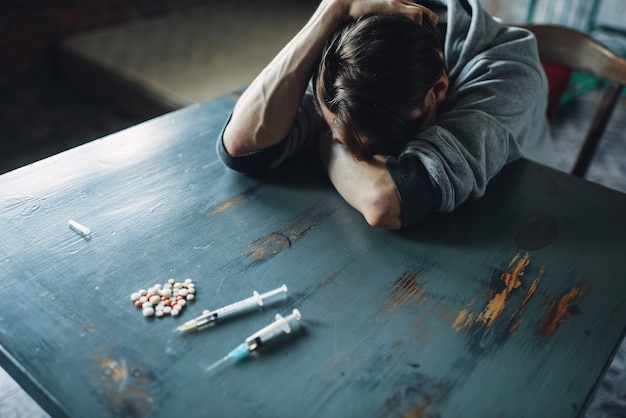 Photo male junkie at the table with drugs and syringe