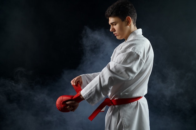 Male karate fighter in white kimono having red belt and gloves, combat stance. Karateka on workout, martial arts, training before fighting competition