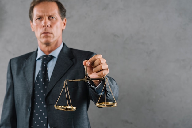 Male lawyer holding golden justice scale against gray textured background