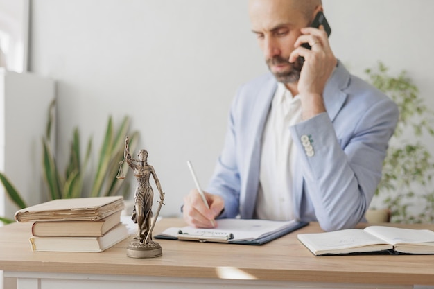 Male lawyer in a white shirt and jacket works in the office a statuette of the goddess of justice