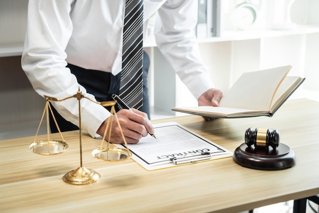 Юрист-мужчина, работающий с судебными контрактными бумажными документами судебного процесса, юридическими книгами и деревянным молотком на столе в офисе.
