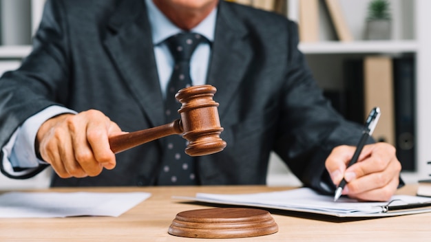 Male lawyer writing on document in a courtroom giving verdict by hitting mallet on gavel