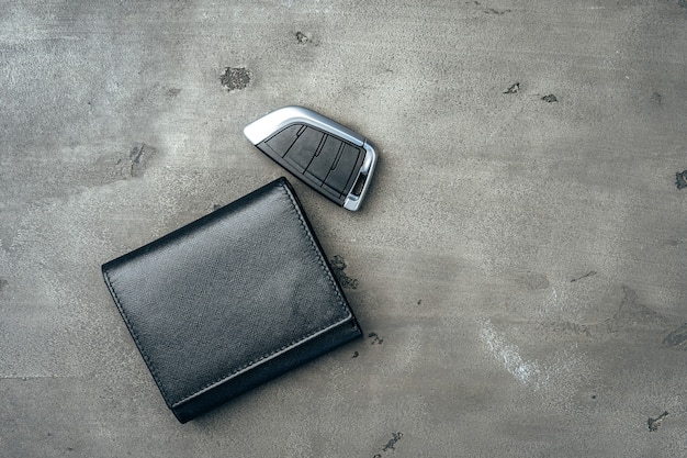 Male leather wallet and car key on dark grey background close up