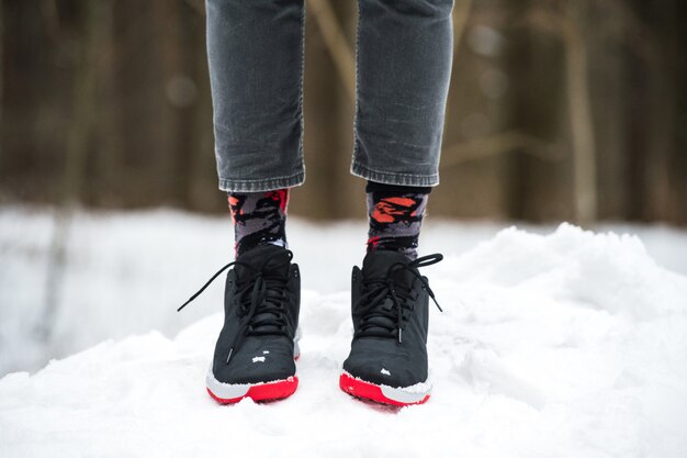 運動靴、トリミングされたジーンズ、雪の上に立っているファッショナブルな靴下の男性の足。