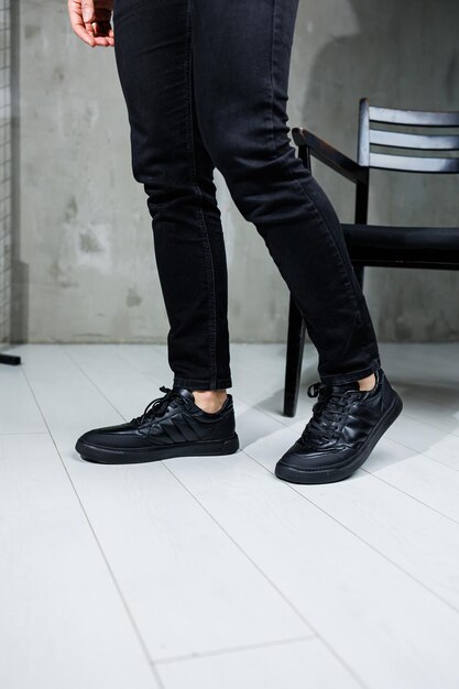 Мужские ноги в черных джинсах крупным планом в черных кожаных повседневных кроссовках Удобная мужская демисезонная обувь