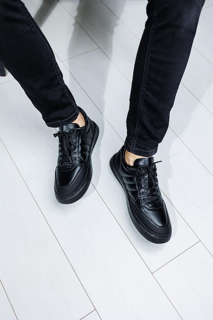 Мужские ноги в черных джинсах крупным планом в черных кожаных повседневных кроссовках Удобная мужская демисезонная обувь
