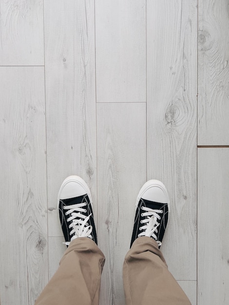 Foto le gambe maschili in scarpe da ginnastica nere si trovano su un pavimento di legno grigio