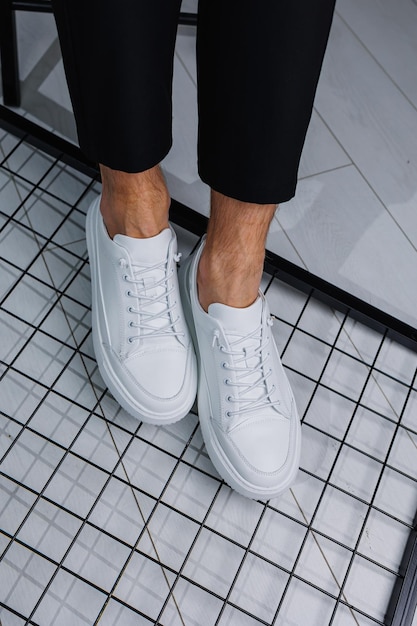 Male legs closeup A man in stylish black pants and white leather sneakers Details of everyday look Men's street fashion