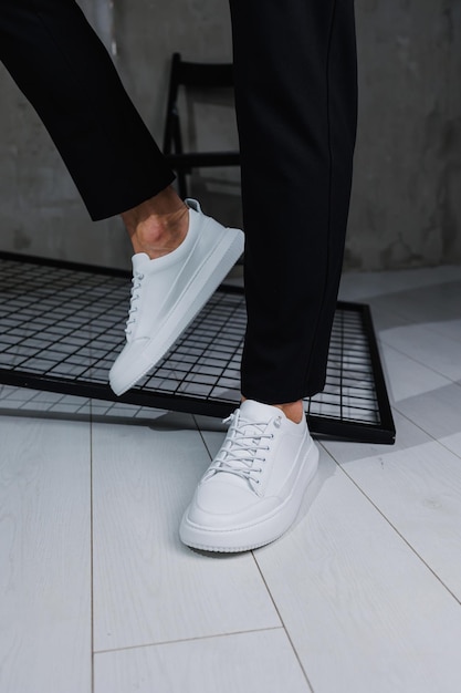 Male legs closeup A man in stylish black pants and white leather sneakers Details of everyday look Men's street fashion