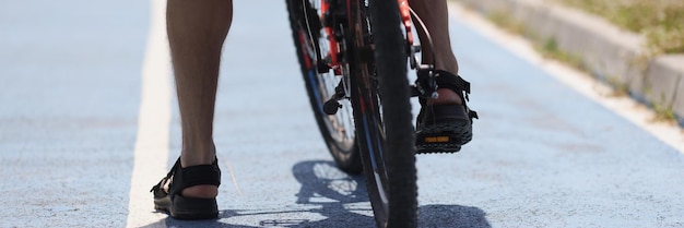 Gambe maschili di un ciclista sulla fermata della bici dell'asfalto