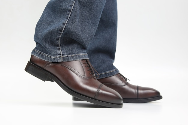 Male legs in jeans and brown classic shoes on white background
