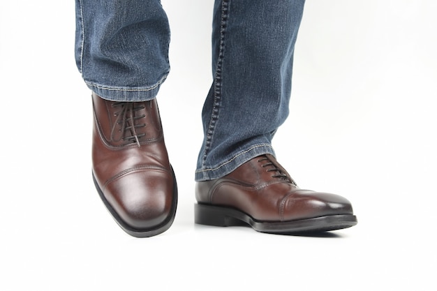 Male legs in jeans and brown classic shoes on white background