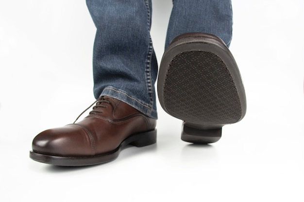 Male legs in jeans and brown classic shoes on white surface