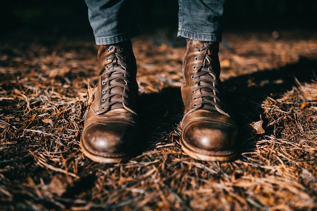 Male legs in trendy leather boots standing in autumn leaves.