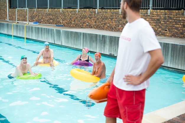 Male lifeguard looking at senior swimmers swimming in pool