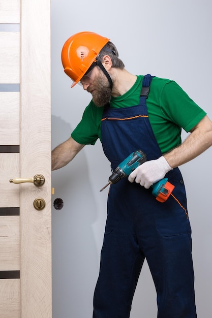 A male locksmith installs a door in an apartment The guy works with a screwdriver