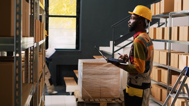 male manager examining products stock with laptop, checking supply chain before doing inventory. depot employee working on quality control for order shipment and delivery in storehouse.
