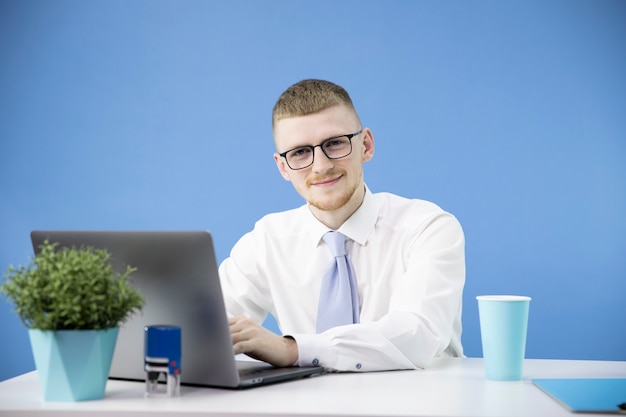 Male manager in office works with laptop smiling accent on blue