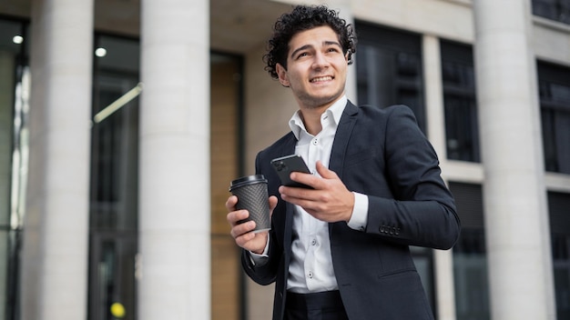 A male manager in an official suit holds a phone in his hands calls a colleague drinks coffee