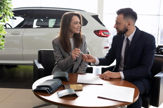 Manager maschio che vende una nuova auto a una giovane donna in un concetto di noleggio auto di concessionaria auto