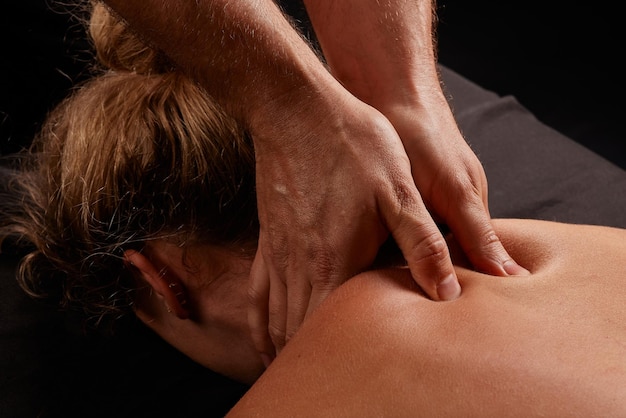 Foto un massaggiatore maschile massaggia il collo di una ragazza su uno sfondo scuro